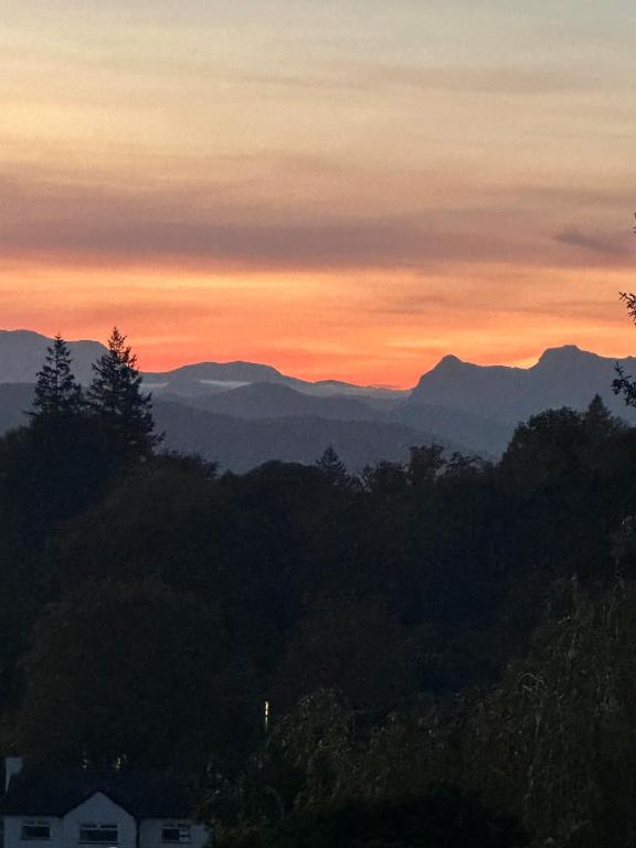 a sunset with mountains in the background and trees at Windermere Hillthwaite Hotel in Windermere