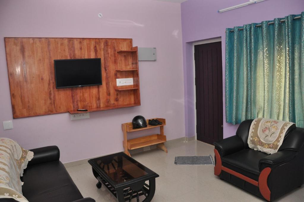 a living room with two chairs and a tv on the wall at Srirangam Service Apartment in Tiruchirappalli