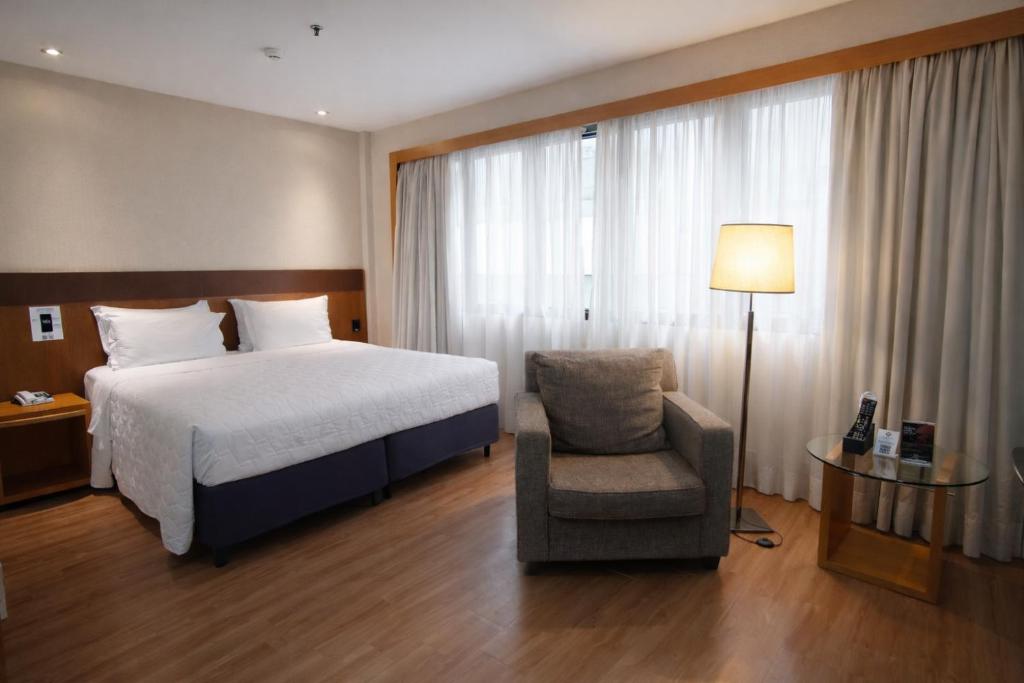 a bedroom with a bed and a chair and a lamp at Transamerica Executive Faria Lima in São Paulo