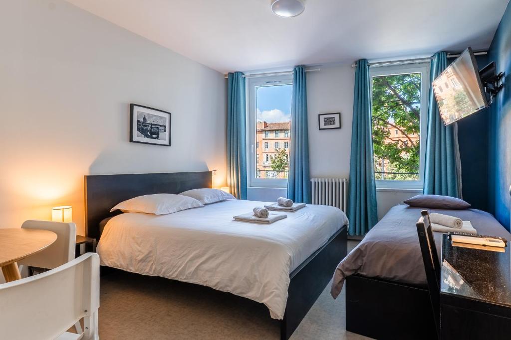 a bedroom with two beds and a table and two windows at Blue Bird - Logement sur les Ramblas in Toulouse