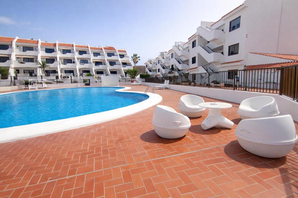 a resort with a swimming pool and white chairs and buildings at Sunny Pool Apartment Costa del Silencio in Arona