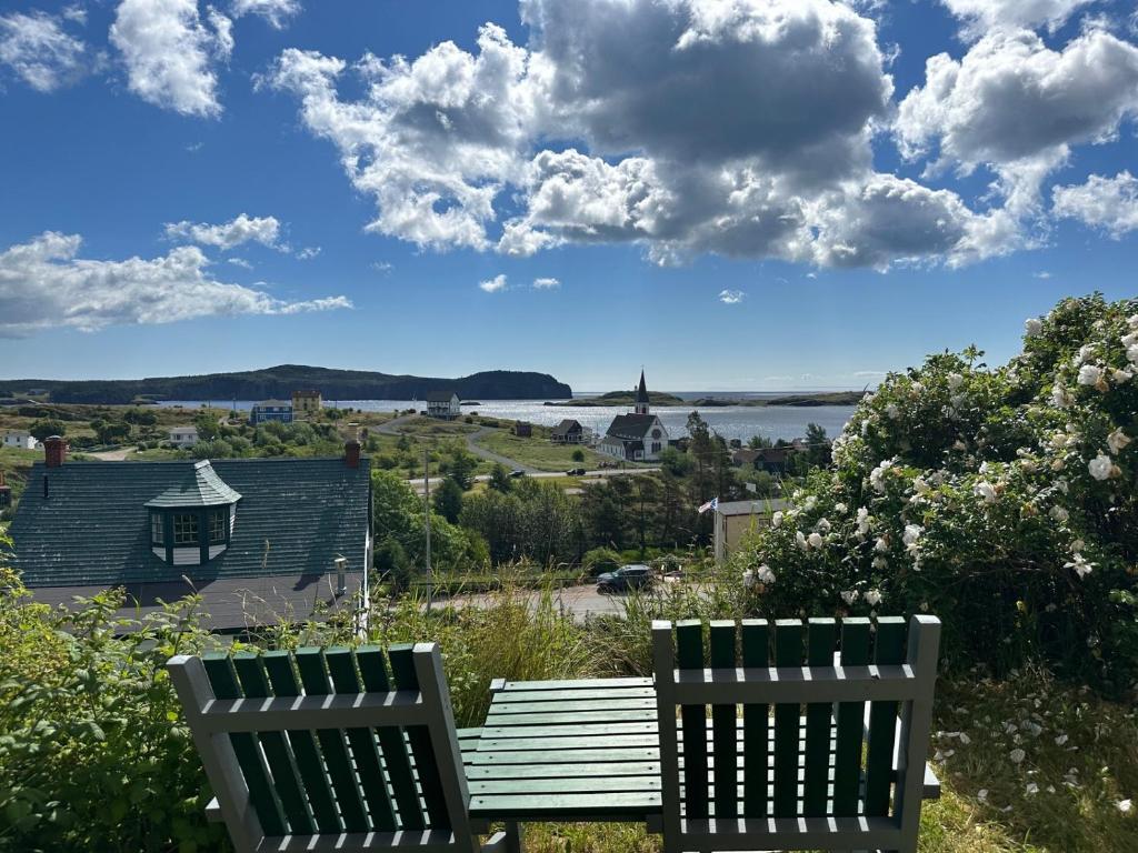 two benches sitting on a hill with a view of the water at Trinity's Oceanview Gem 2BR St Paul's Schoolhouse in Trinity