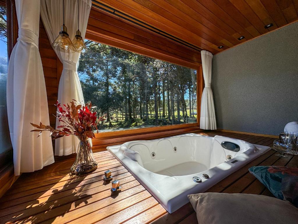 a bath tub in a room with a large window at Villa Vida Cabanas in São Joaquim