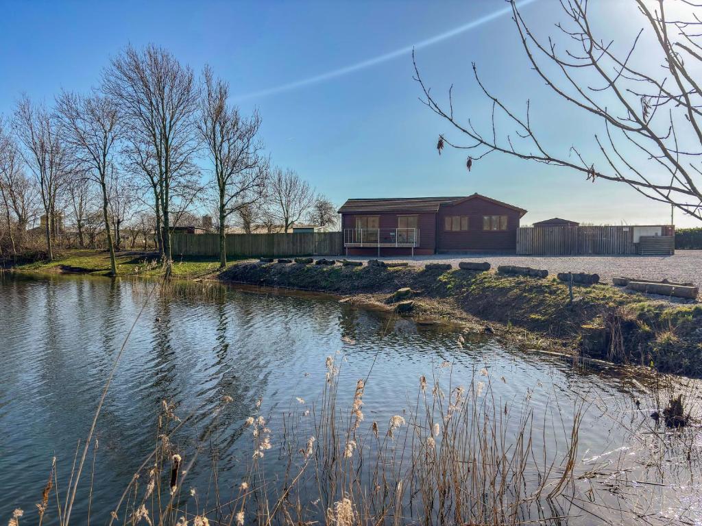 a house on the side of a river with a building at Star Carr Lakes in Great Driffield