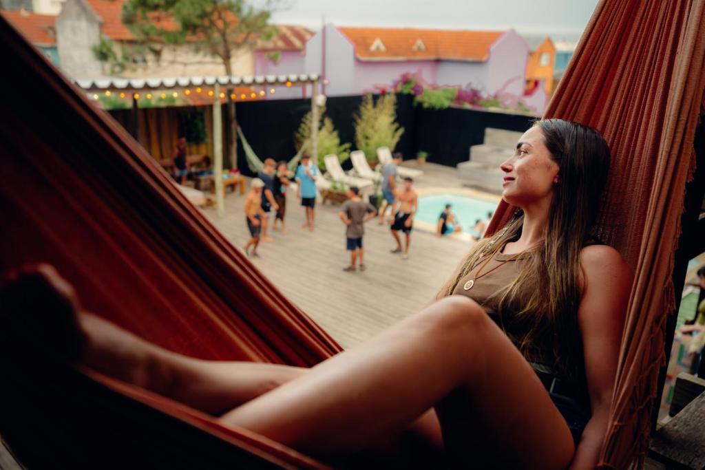 a woman sitting in a hammock in front of a pool at Compay Hostel Punta del Diablo in Punta Del Diablo