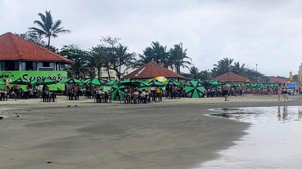 a beach with green umbrellas and people on the beach at Casinha marazul in Itanhaém
