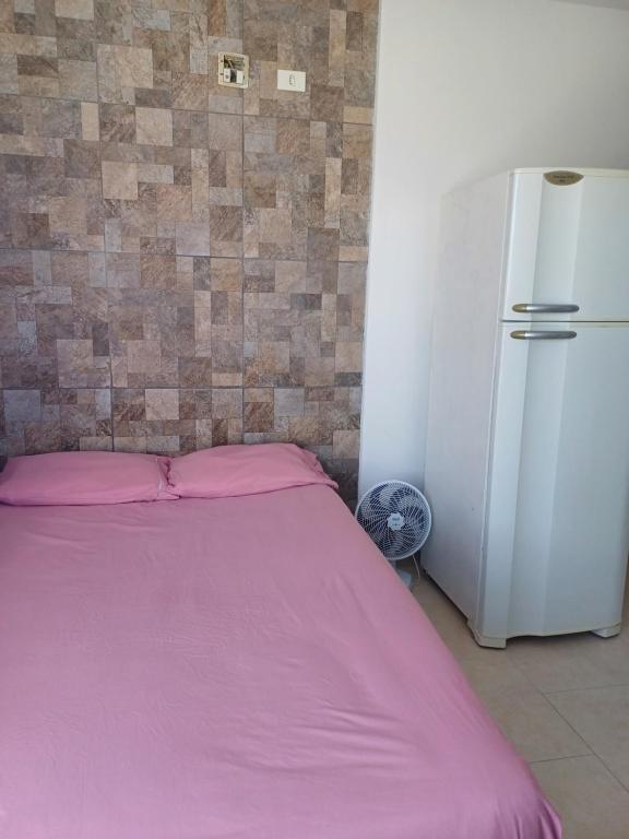 a bed with a pink blanket next to a refrigerator at Suíte praia de leste in Pontal do Paraná