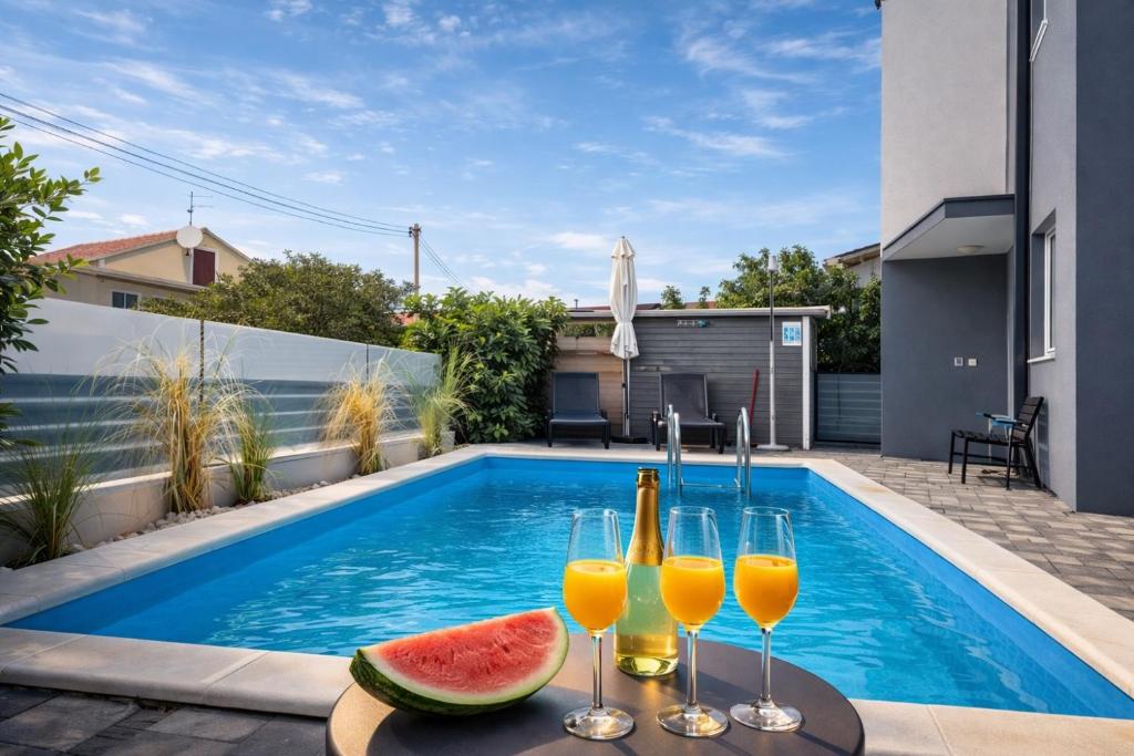 a pool with two glasses of orange juice and watermelon at Luxury Apartment Lukas Pool & Parking Vodice in Vodice