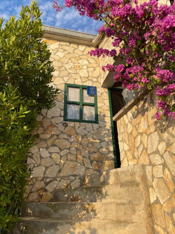 a stone house with a window and purple flowers at Robinzonska kuća uz more in Tkon