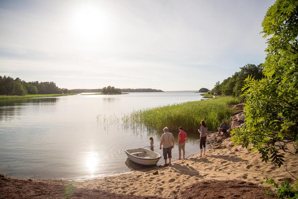 Villa Kommodor في Lumparland: مجموعة من الناس تقف على شاطئ بجوار قارب