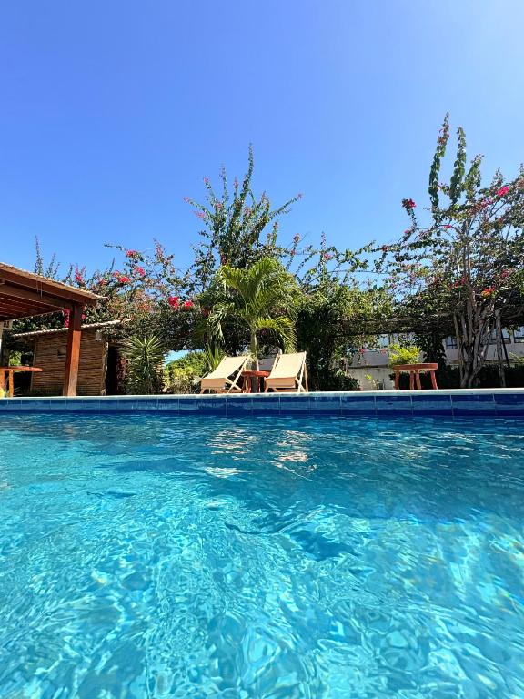 a swimming pool with blue water and chairs and trees at POUSADA RANCHO PARAISO in Pôrto de Pedras