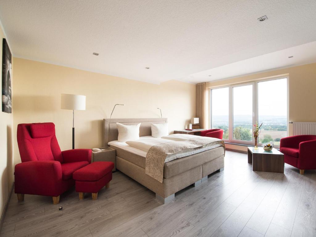 a bedroom with a bed and two red chairs at Design-Konferenzhotel & Restaurant Steinernes Schweinchen in Kassel