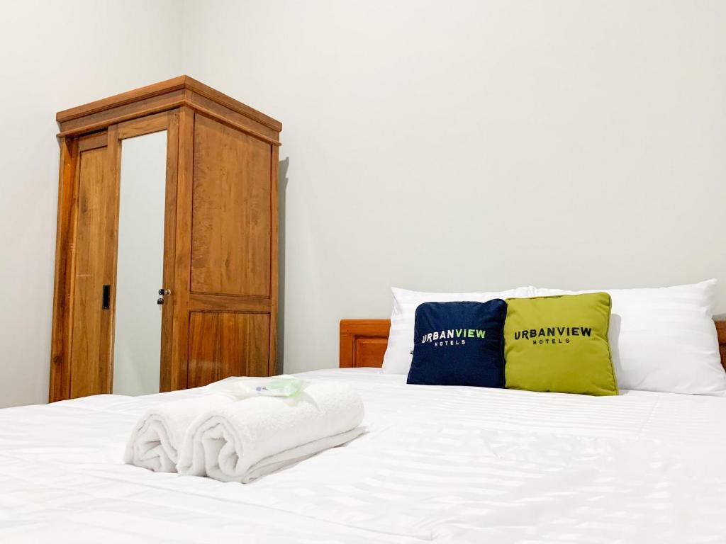 a bed with white sheets and pillows on it at Urbanview Hotel The Corner Pandowo in Ngaglik
