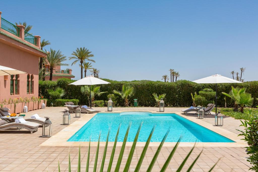 La Palmeraie De L'Atlas في مراكش: مسبح بكراسي ومظلات بجانب بيت