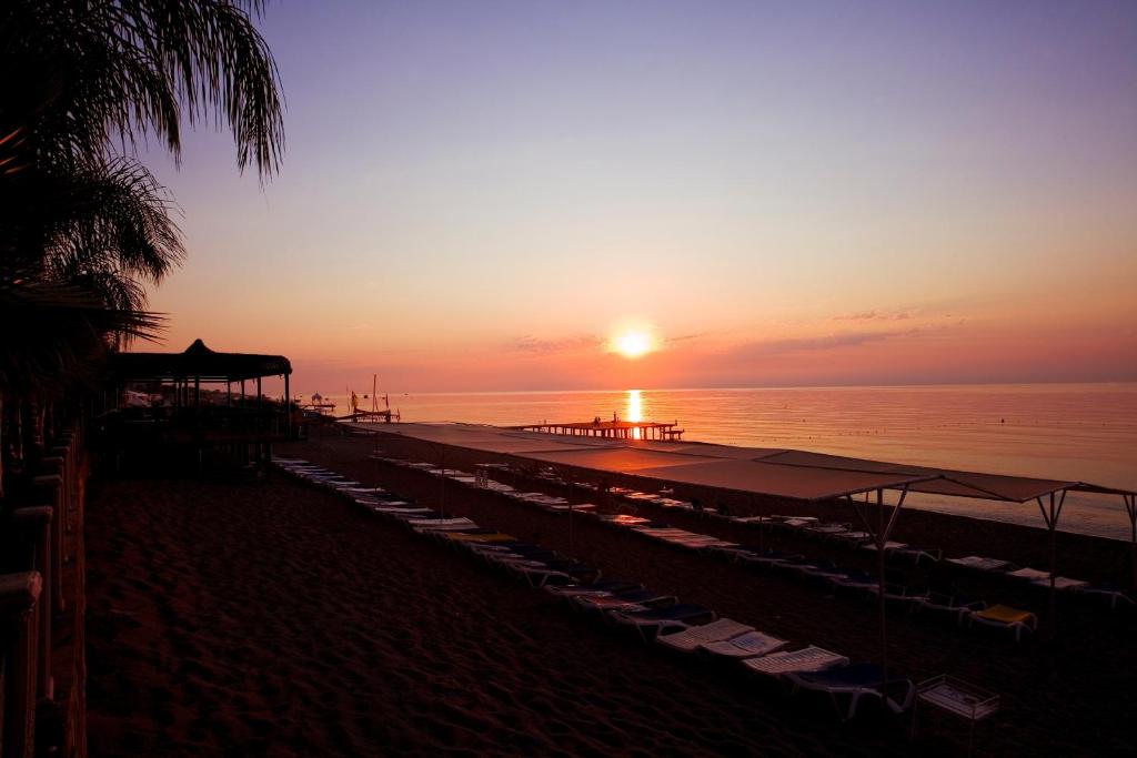 a sunset on a beach with umbrellas and the ocean at Marvıda Hotel Akman Park in Kemer