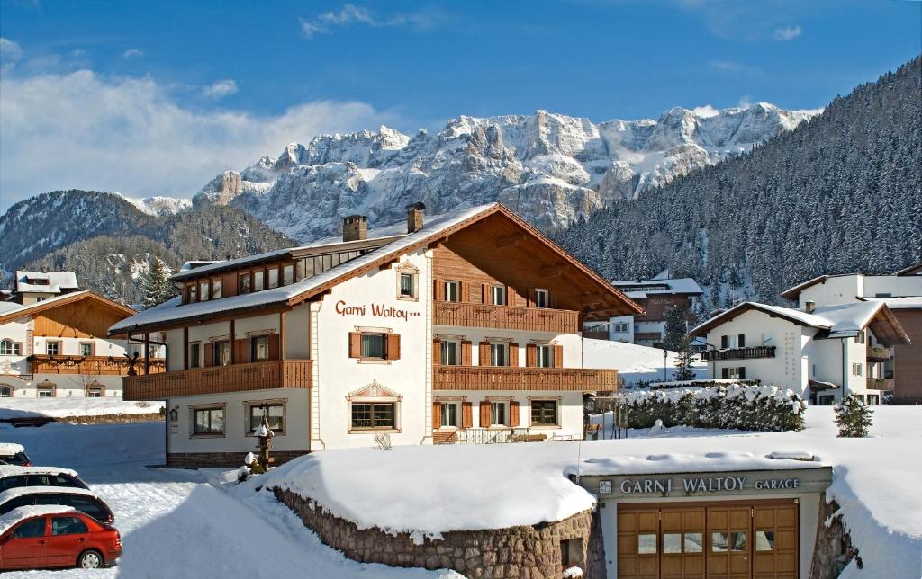 a building in the snow with mountains in the background at Garni Waltoy in Selva di Val Gardena