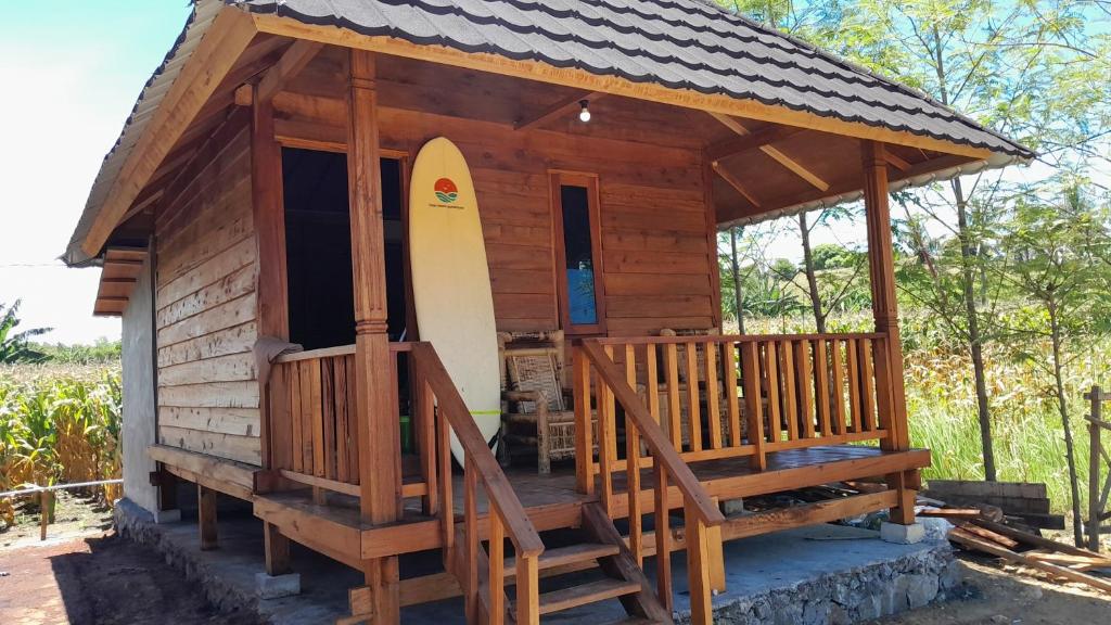 a small wooden cabin with a surfboard on the porch at anisa homestay and restaurant in Ekas