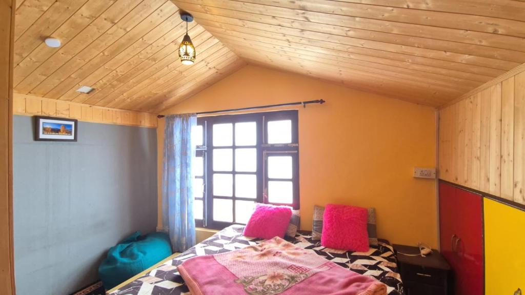 a bedroom with a bed with pink pillows and a window at Beyond Rohtang in Tāndi