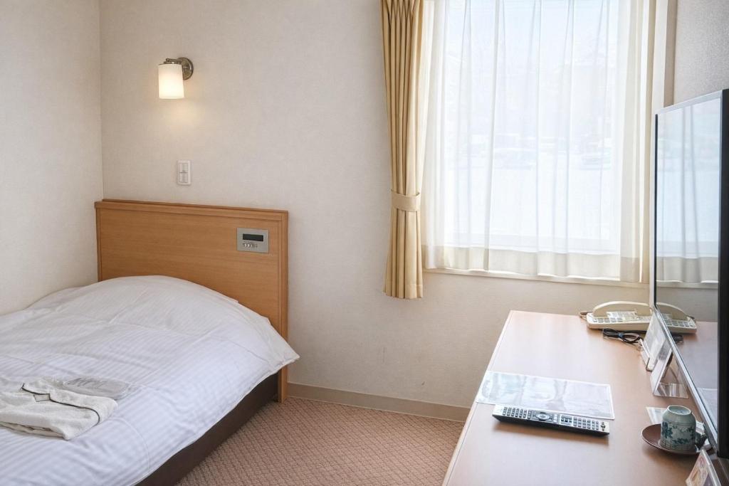 a hotel room with a bed and a desk and a window at Tetora Higashimuroran in Muroran