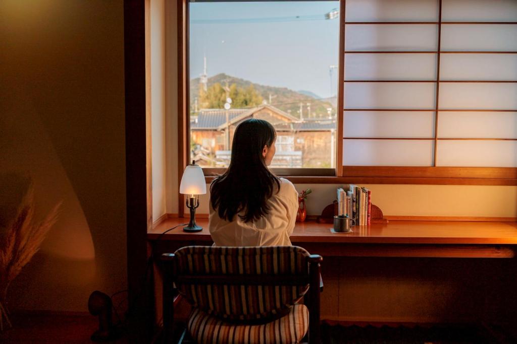 a woman sitting in a chair looking out a window at めぐり宿 庵結 in Shimonoseki