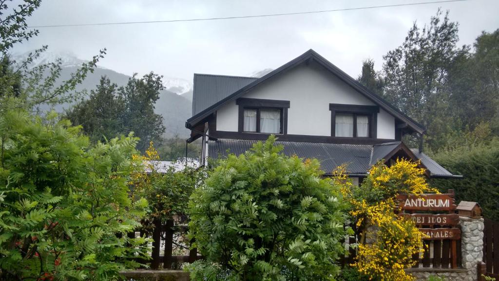 una casa en blanco y negro con árboles delante en Las Rosas Alojamiento Turistico en Villa La Angostura