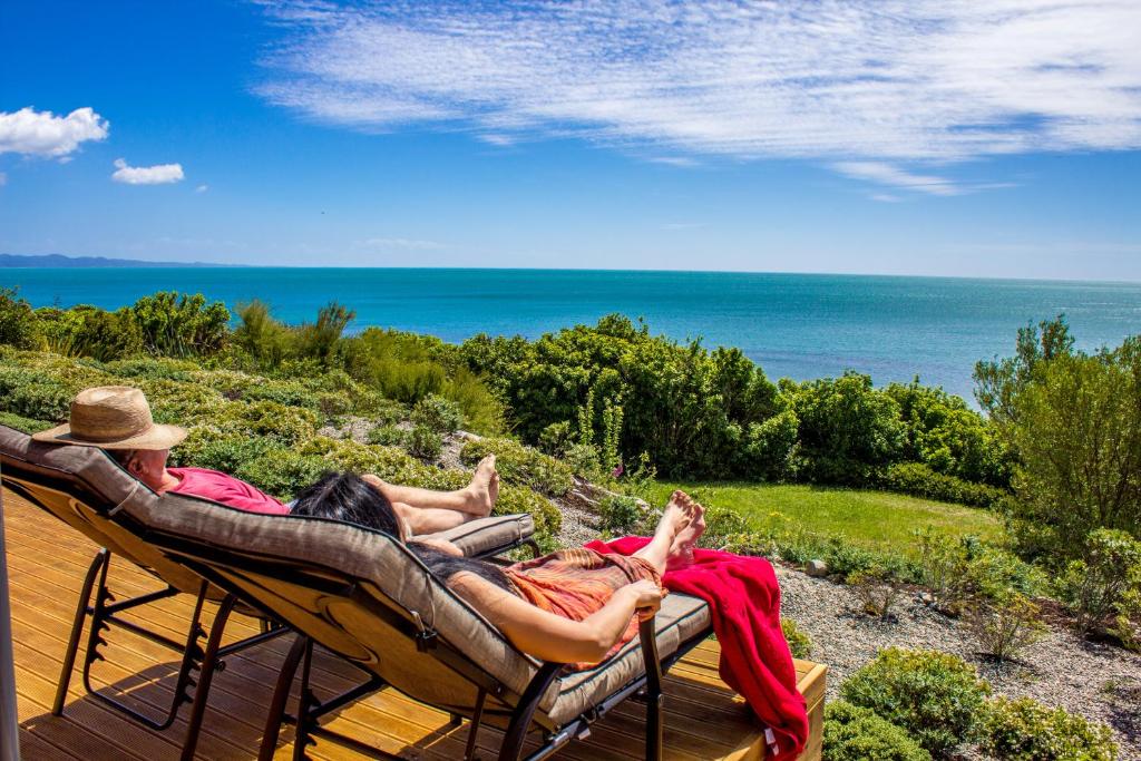 two people laying in hammocks on a deck overlooking the ocean at Sunrise Apartment - Golden Bay in Onekaka