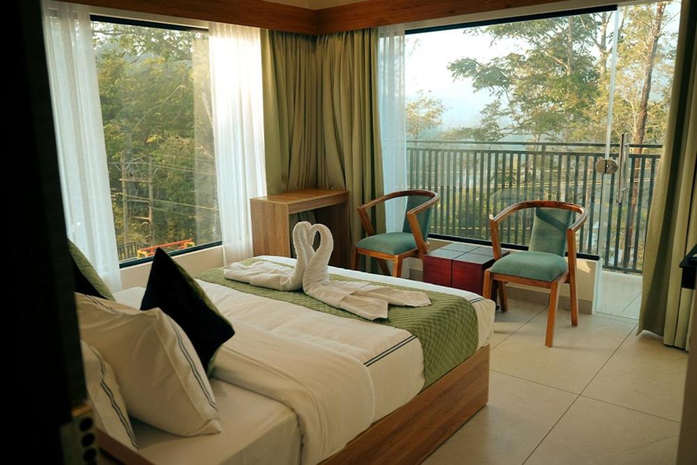 a bedroom with a bed and two chairs and a balcony at Lazo EcoSpot Vythiri , Wayanad in Vythiri