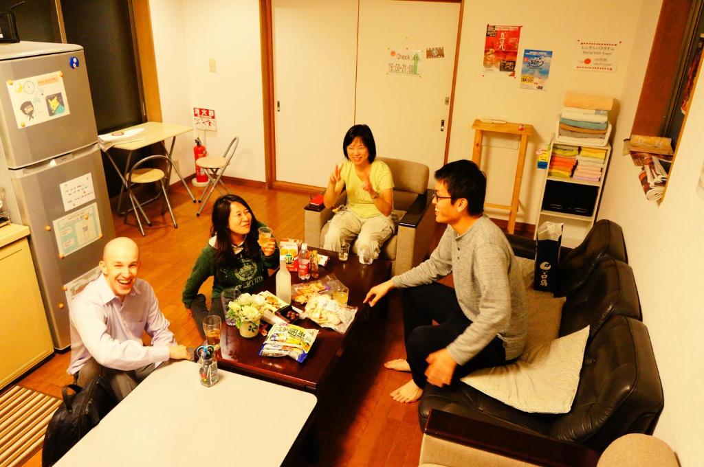 um grupo de pessoas sentadas à volta de uma mesa numa sala em Osaka Tomato Guesthouse em Osaka
