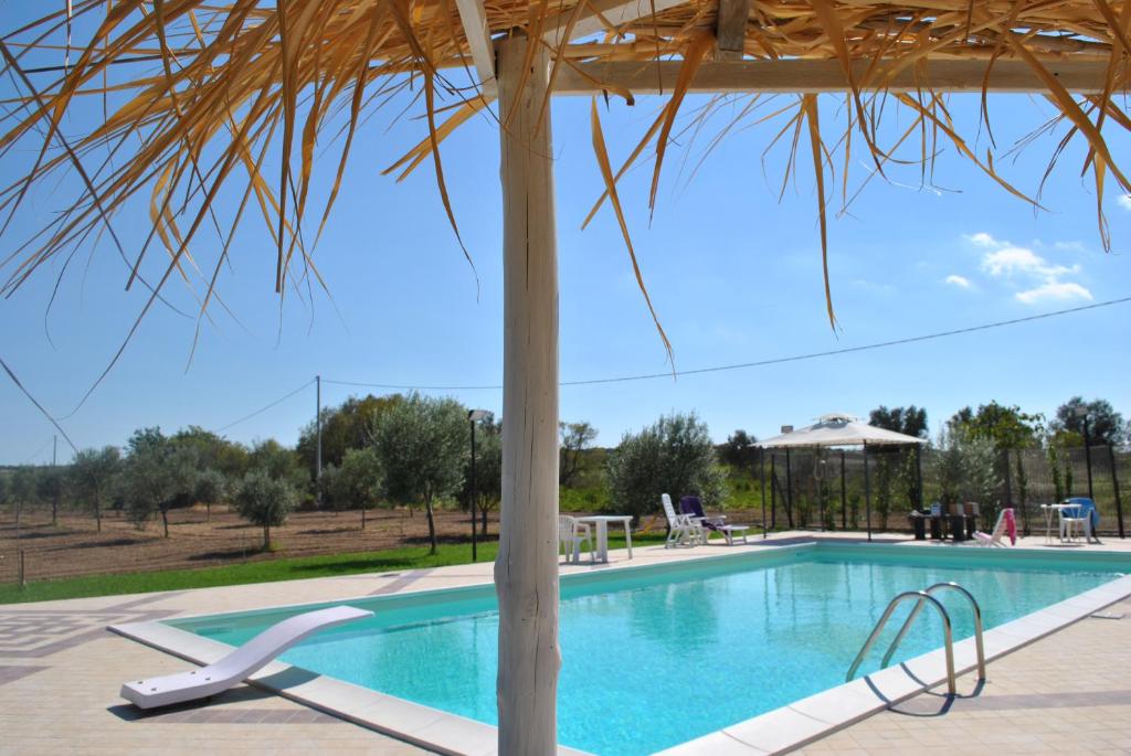 una piscina con sombrilla de paja y un complejo en Agriturismo Agrimaccari Marzamemi-Vendicari - Esperienza autentica siciliana, en Marzamemi