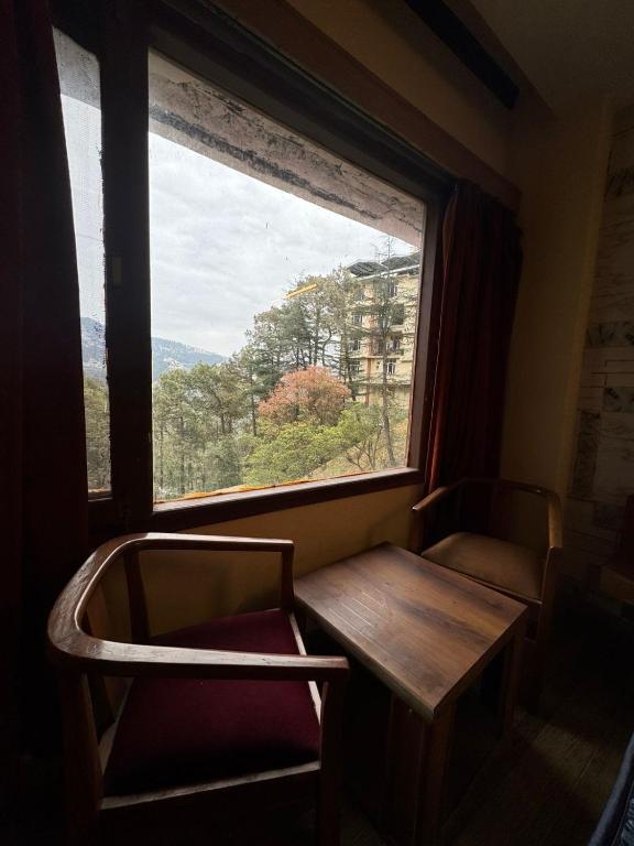 a table and chairs in a room with a window at Hotel Sham Ji in Chhota Simla