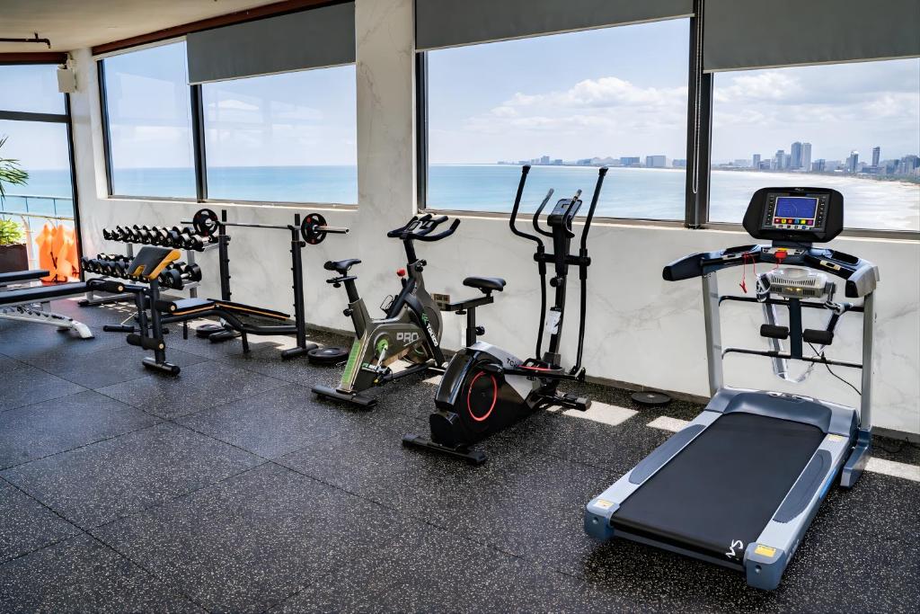A bright hotel gym with cardio and strength equipment overlooking the sea.