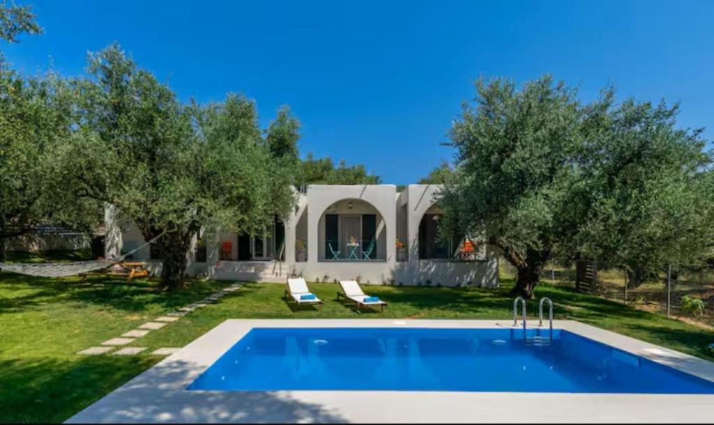 a swimming pool in front of a house with trees at Vardavilla in Lithakia