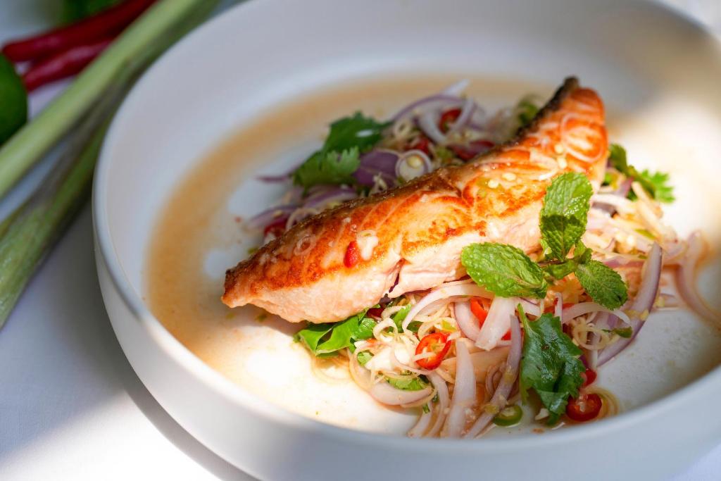 A plated salmon dish served over noodles or salad with herbs, onion and chillies.