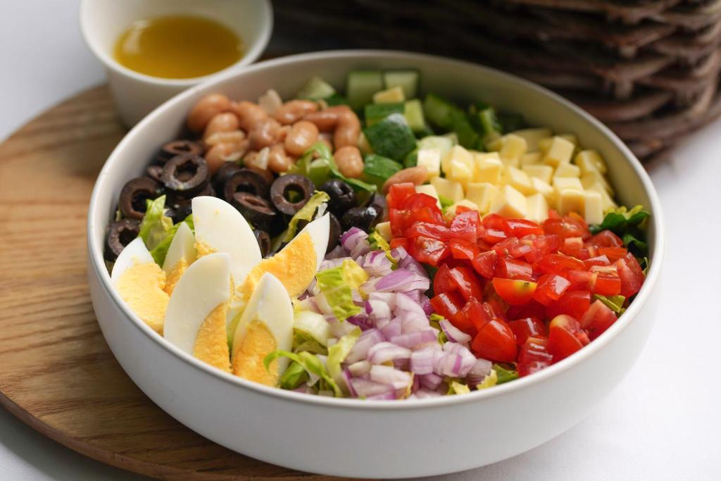 A colourful salad bowl with eggs, beans, cheese, olives, tomatoes and mixed vegetables.