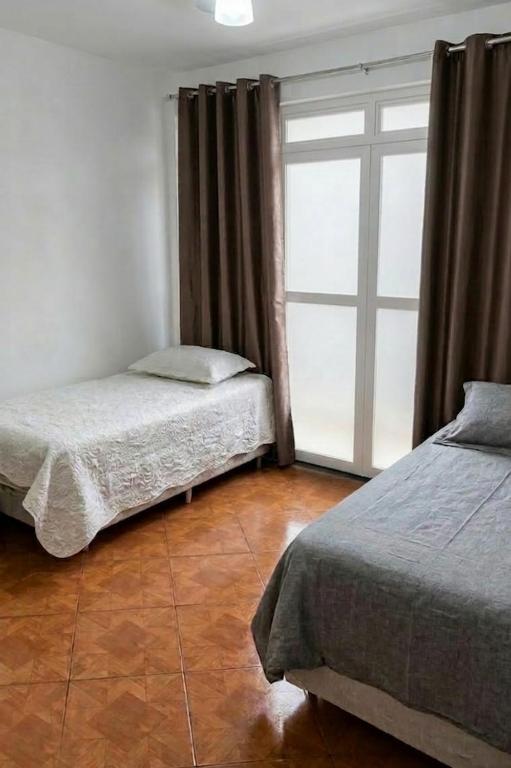 a bedroom with two beds and a large window at Quarto individual Aconchego in Divinópolis