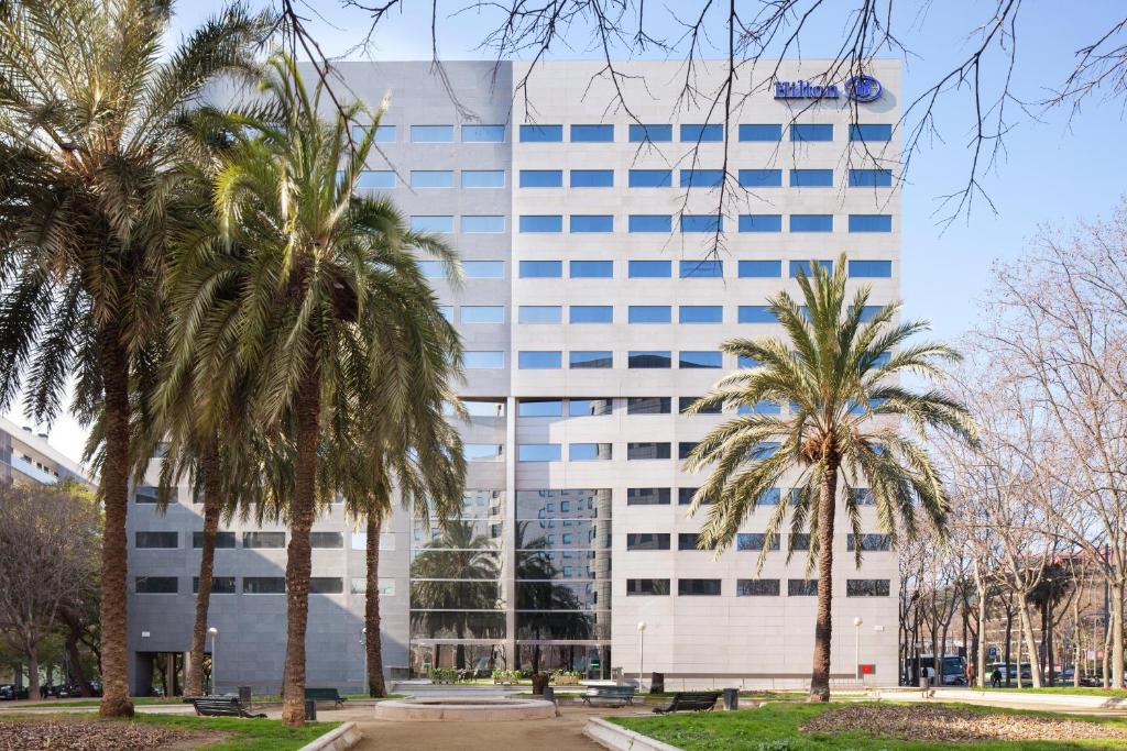 a tall building with palm trees in front of it at Hilton Barcelona in Barcelona
