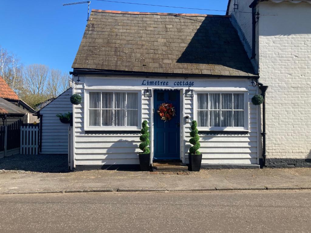 a white house with a blue door on a street at Lime Tree Cottage in Tillingham
