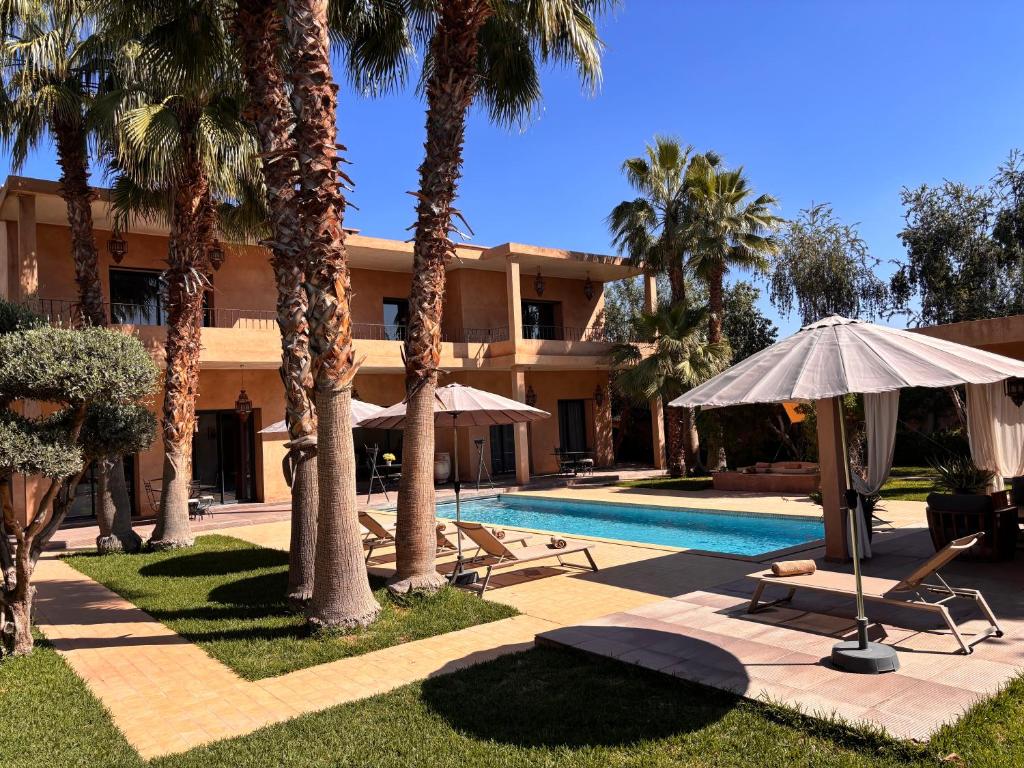 a resort with a pool and palm trees and an umbrella at villa Bidouane in Marrakesh