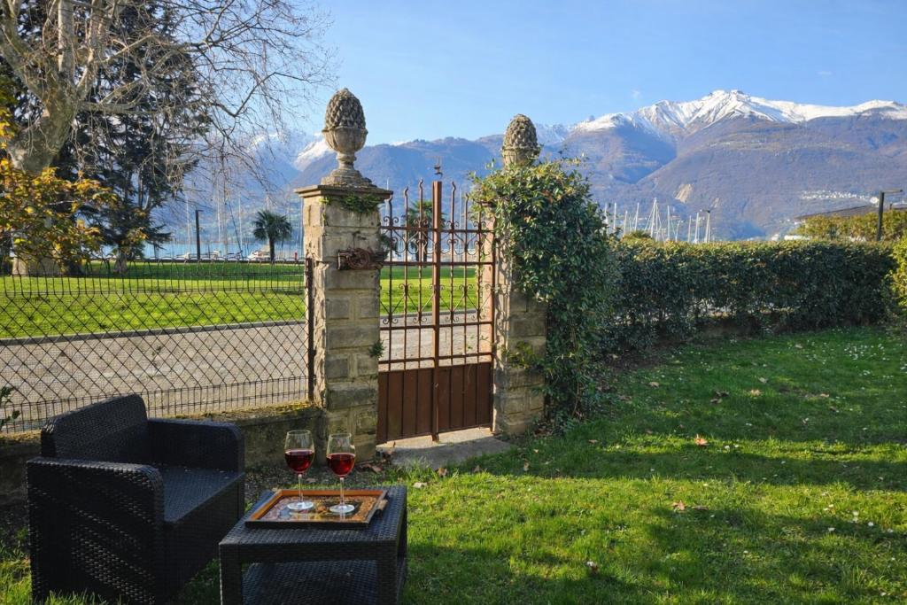 a fence with a gate and a table with two glasses of wine at Villa Lago Groundfloor Lakefront Beach Garden Bike&Boat& Scooter Lake Como in Colico