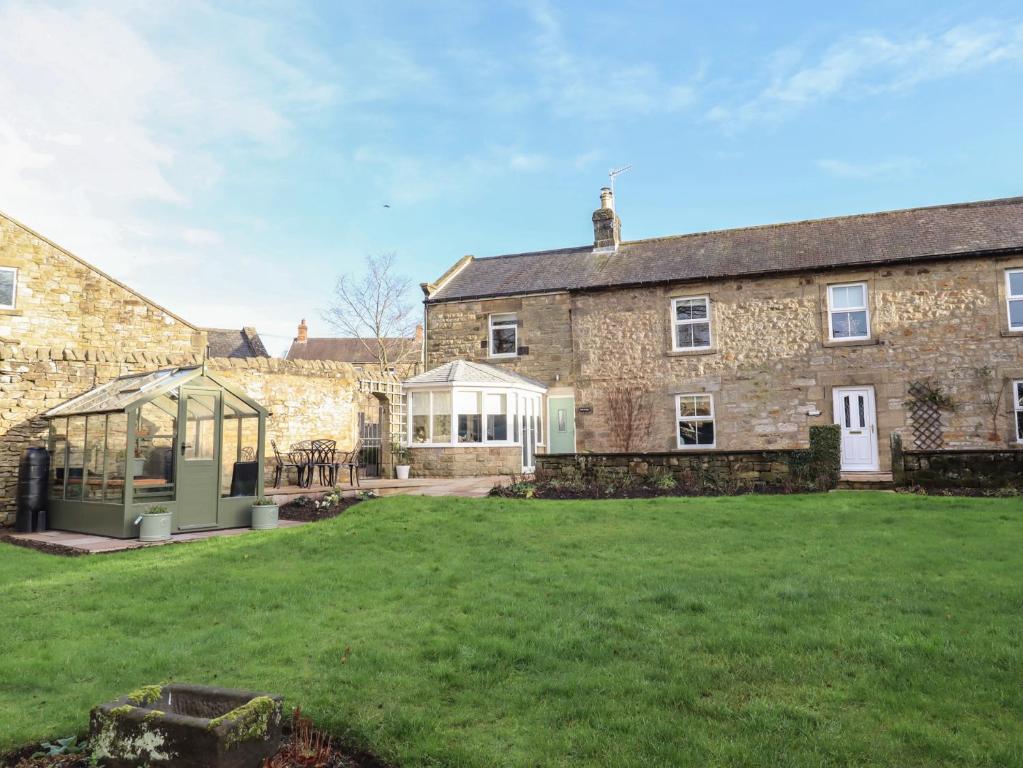 an old stone building with a greenhouse in the yard at Linn Cottage in Hexham