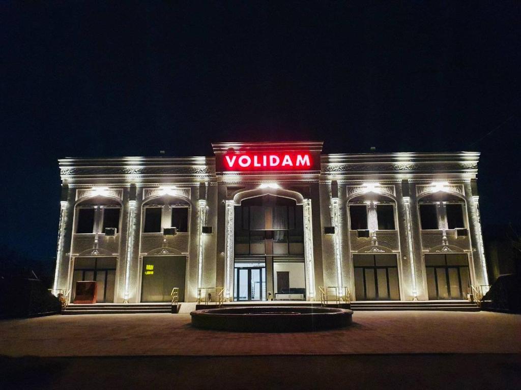 a white building with a red neon sign on it at Volidam Hotel in Qarshi