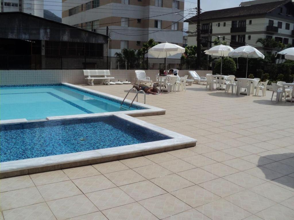 a swimming pool with chairs and tables and umbrellas at Apto novo com ampla sacada e piscinas in Guarujá