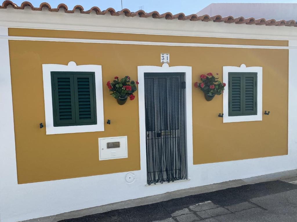 a yellow building with green shutters and flowers on it at Casinha Amarela in Cabeção