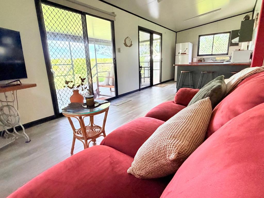a living room with a red couch and a table at Feng Shui Sugarcane Cabin in Proserpine