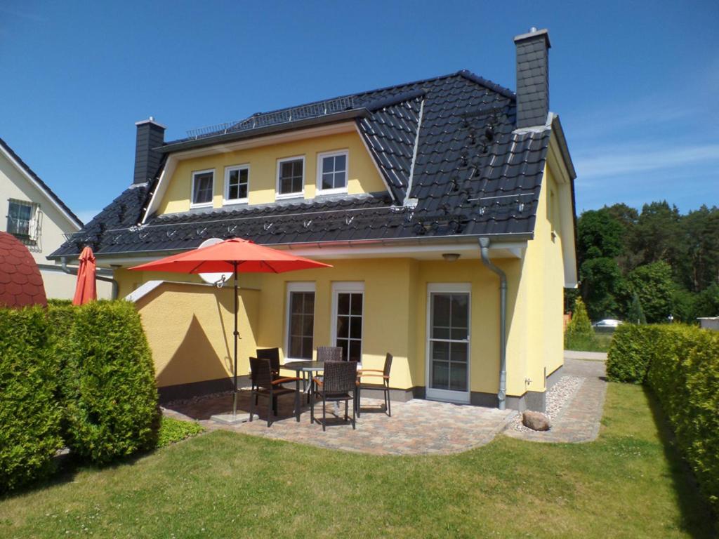 uma casa amarela com uma mesa e cadeiras e um guarda-sol em Ferienhaus am Eikboom - DHH2 mit Fasssauna em Ostseebad Karlshagen