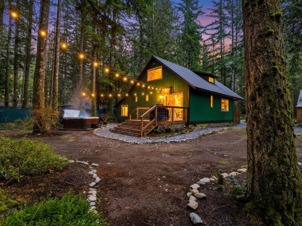 a green cabin in the middle of a forest with lights at Ravens Retreat in Index