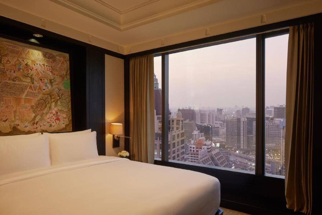 A king bed beside a full-height window overlooking Bangkok’s evening skyline.