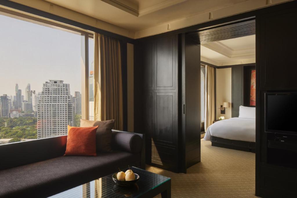 A dark-toned sitting area opening toward a bed and broad city view.