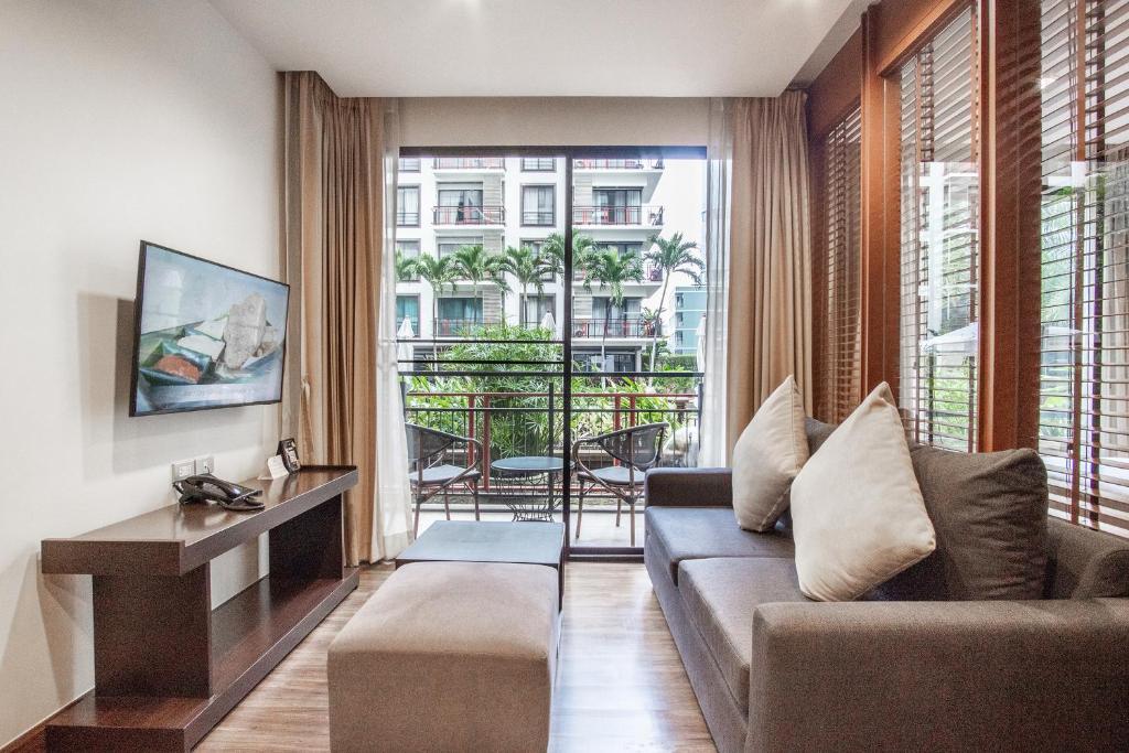 A bright living room with a sofa, television console, ottoman, and glazed balcony.