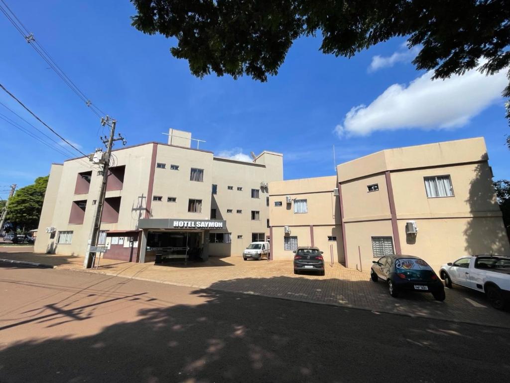 a building with cars parked in a parking lot at HOTEL SAYMON - Cafelândia PARANÁ in Cafelândia